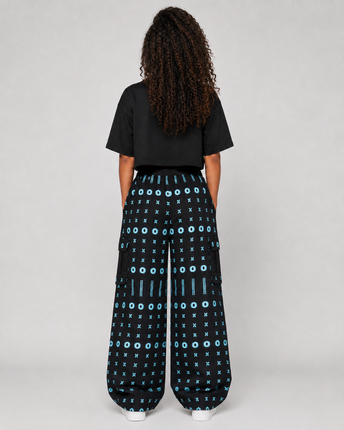 A model viewed from the back wearing a black t-shirt and black wide-leg pants with a light blue geometric pattern, set against a plain light gray background.