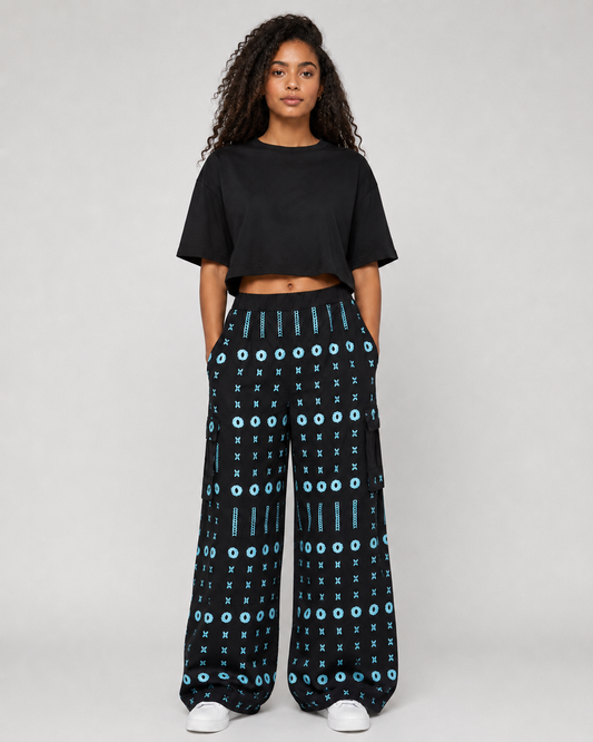A model wearing a black short-sleeve crop top and black wide-leg pants with a blue geometric pattern, standing against a light gray studio background.