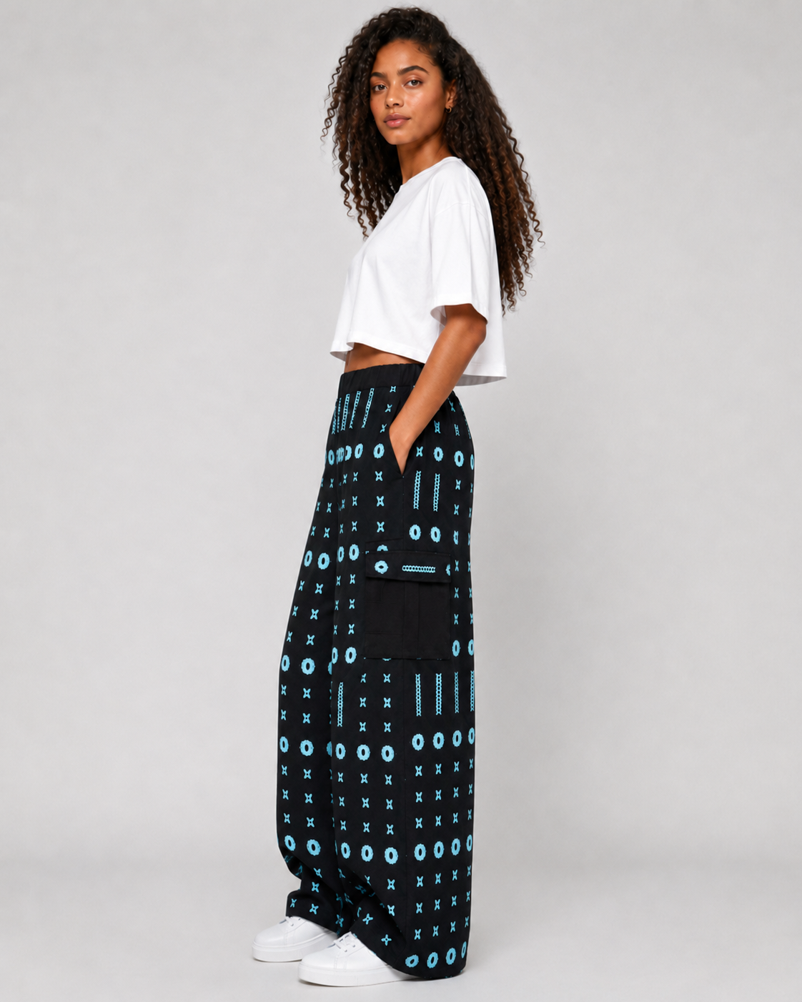 A model wearing a white cropped t-shirt and black wide-leg pants with a light blue geometric pattern, standing against a light gray studio background.