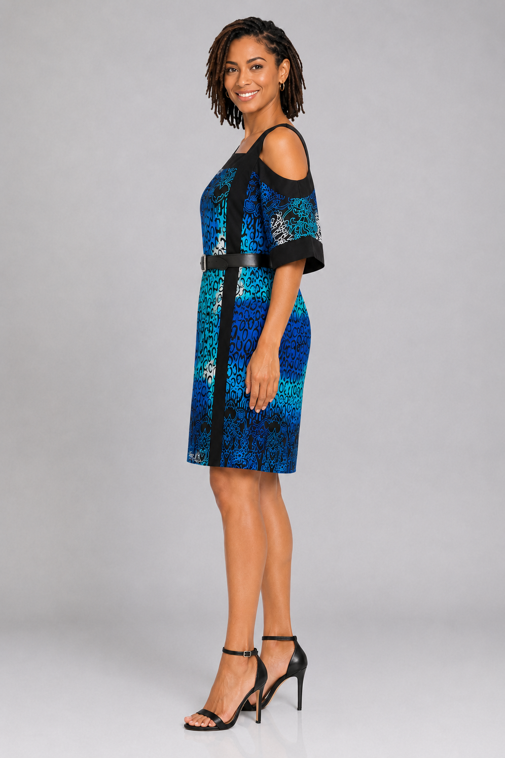 A woman modeling a blue and black patterned cold-shoulder mini dress with a matching black belt, paired with black high-heeled sandals, against a light gray studio background.