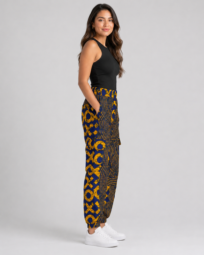 A woman modeling high-waisted, wide-leg pants with a bold yellow and dark blue geometric pattern, paired with a black sleeveless top and white sneakers, against a light gray studio background.