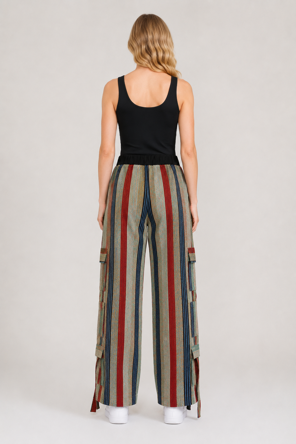 A woman shown from the back wearing a black tank top and wide-leg striped pants with vertical red, blue, beige, and gray stripes, standing against a light gray studio background.