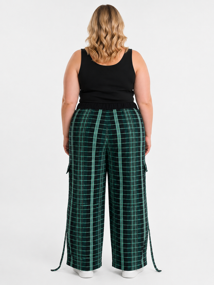 A woman shown from the back wearing dark green wide-leg plaid pants with a black tank top, against a light gray studio background.