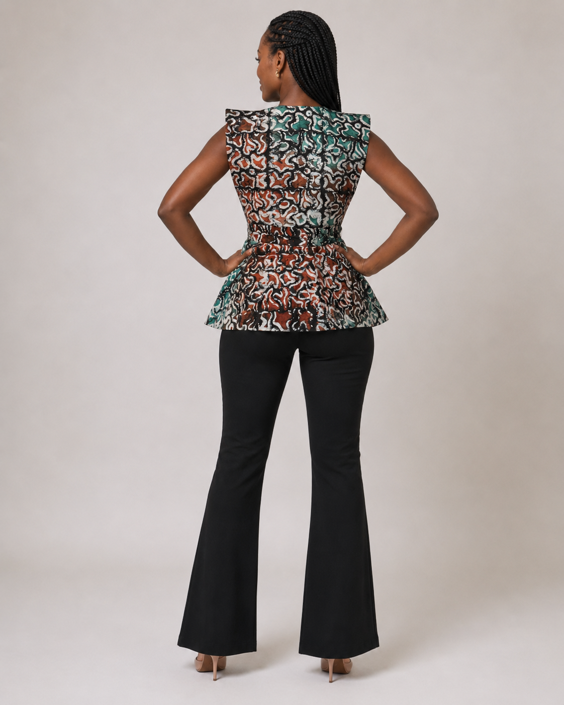 A woman is shown from the back wearing a sleeveless peplum top with a multicolor abstract pattern and black flared pants, standing against a plain light gray studio background.