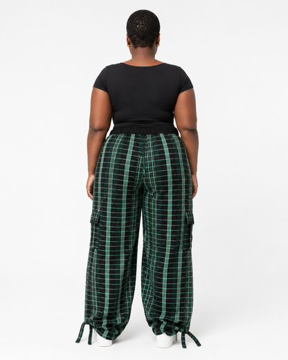 A model viewed from the back wearing wide-leg green and black plaid cargo pants with a black short-sleeve top, set against a plain white studio background.