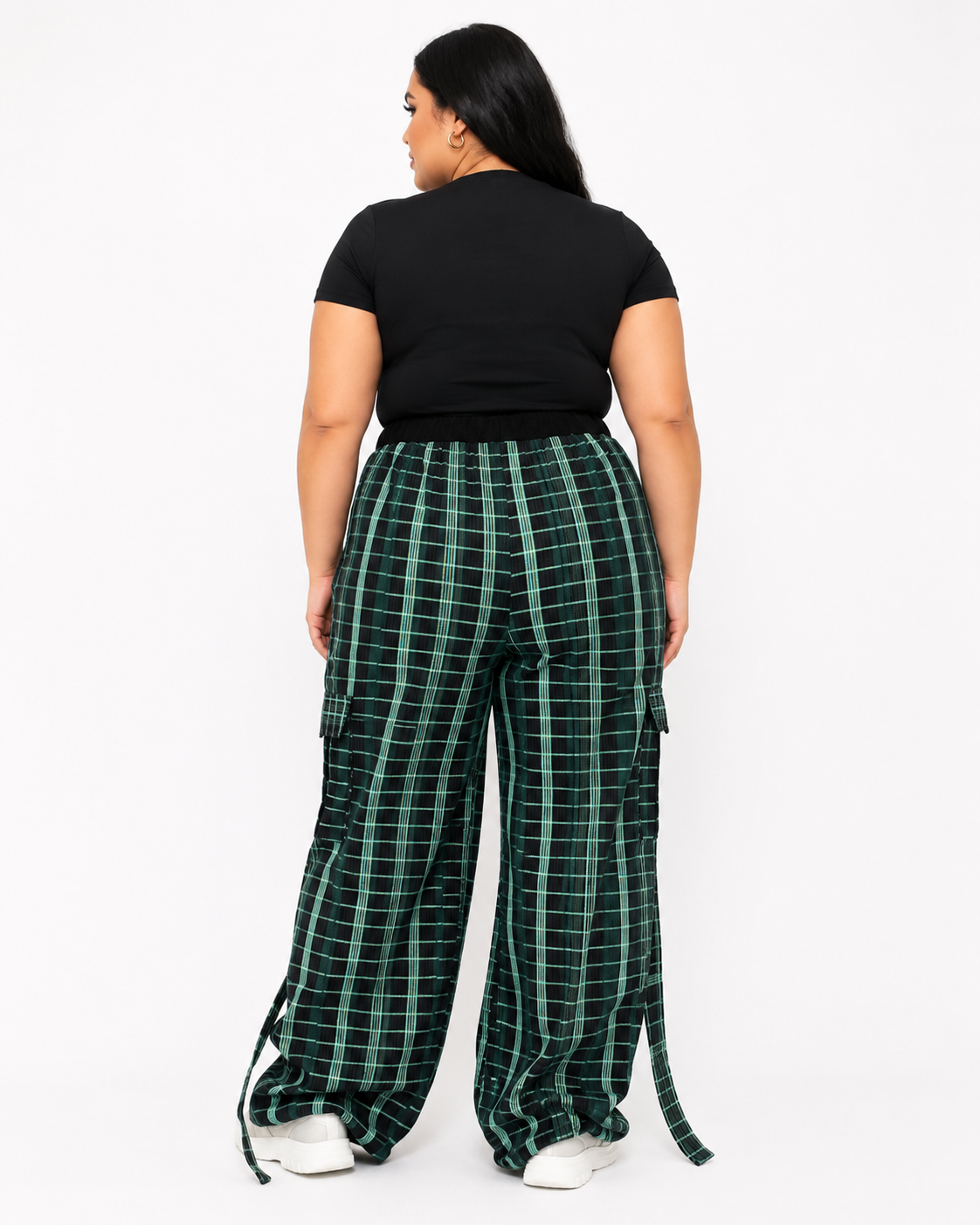 A model shown from the back wearing green and black plaid wide-leg cargo pants with a black t-shirt and white sneakers, set against a plain white studio background.