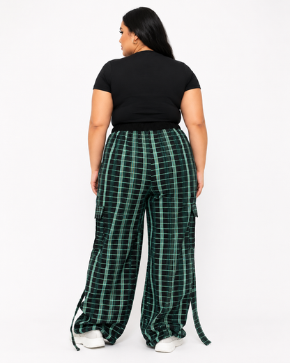 A model shown from the back wearing green and black plaid wide-leg cargo pants with a black t-shirt and white sneakers, set against a plain white studio background.