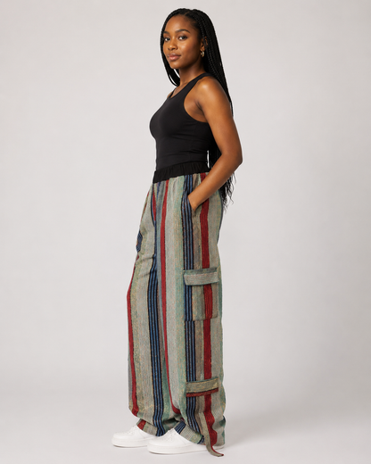 A woman modeling wide-leg striped cargo pants with a black tank top and white sneakers, standing against a light gray studio background.