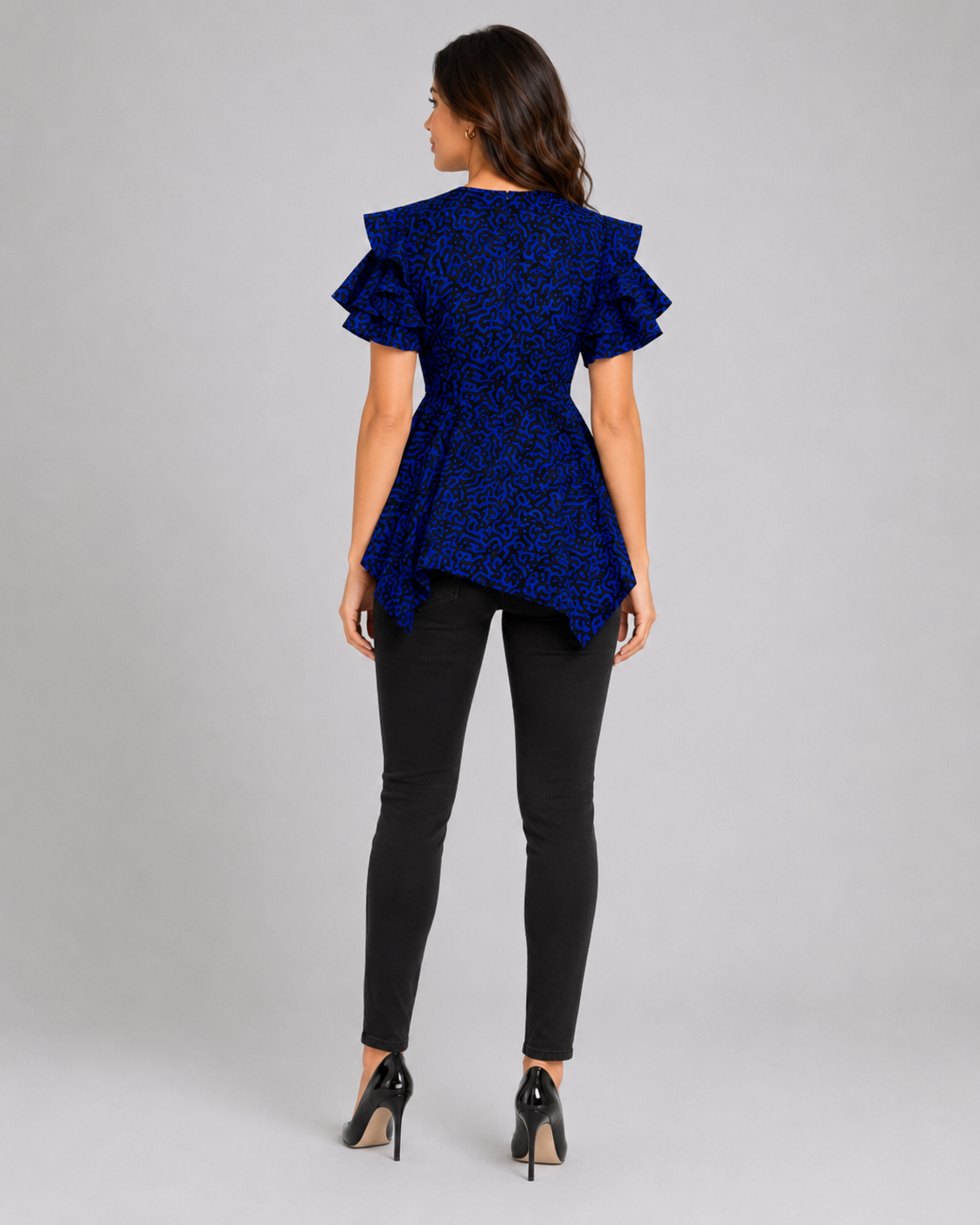 A woman shown from the back wearing a royal blue lace ruffled short-sleeve top, black skinny pants, and black high heels against a light gray studio background.