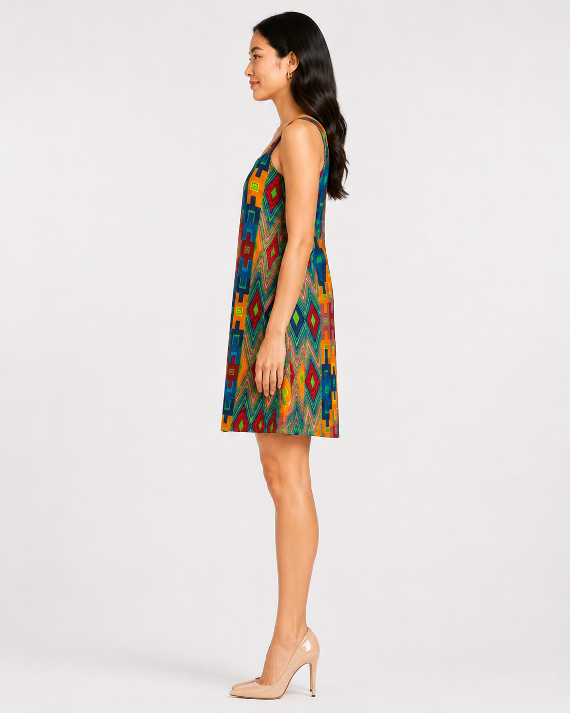 A woman modeling a sleeveless A-line mini dress with a vibrant multicolor geometric pattern, shown in profile against a plain light gray studio background.